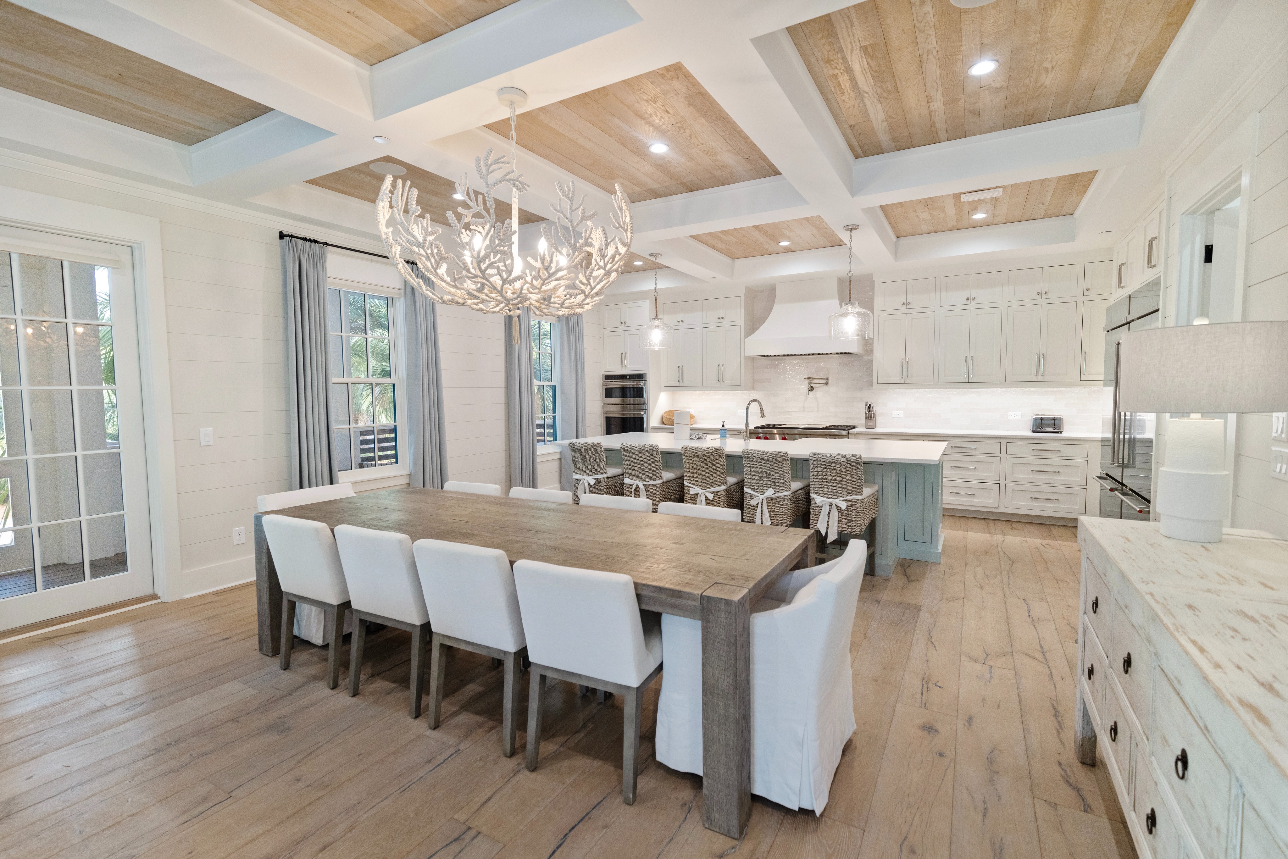 Gather around this spacious dining table where meals become memories. The coffered ceiling, coastal-inspired chandelier, and open-concept design invite you to cook, dine, and connect in elegance.