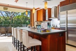 Picture yourself preparing meals in this gourmet kitchen with elegant wood cabinetry, stainless steel appliances, and a breakfast island—all opening to lush tropical views beyond.