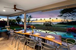 Outdoor dining area overlooking a tranquil pool and ocean at dusk.