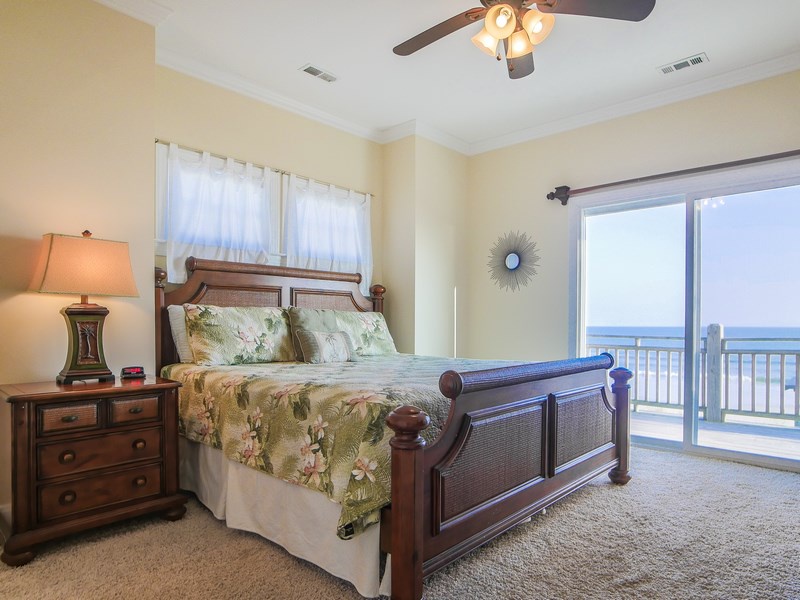 The primary bedroom with a king-sized bed, flat-screen TV, and oceanfront balcony access
