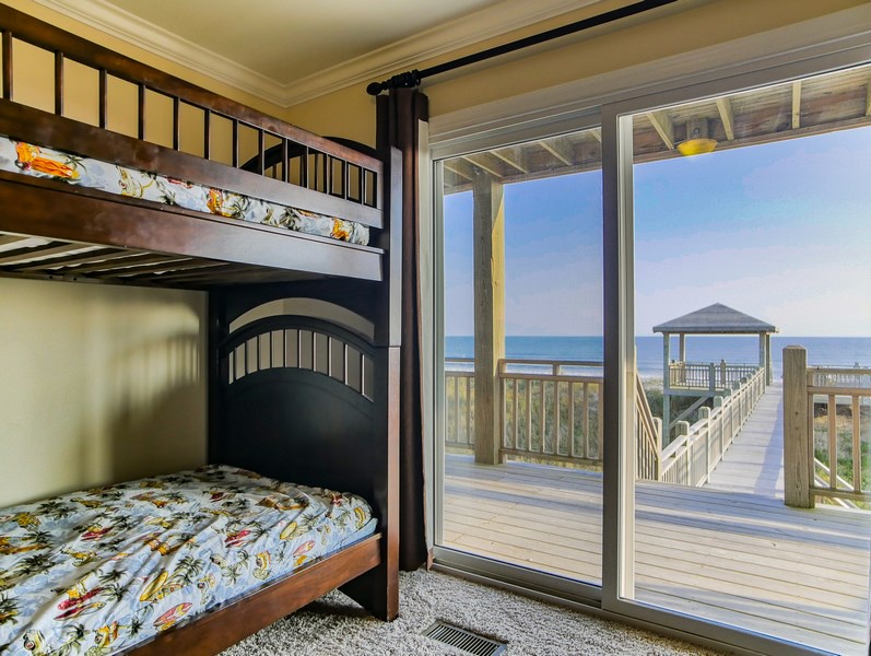 First floor guest bedroom with two twin bunk beds, flat-screen TV, and oceanfront deck access