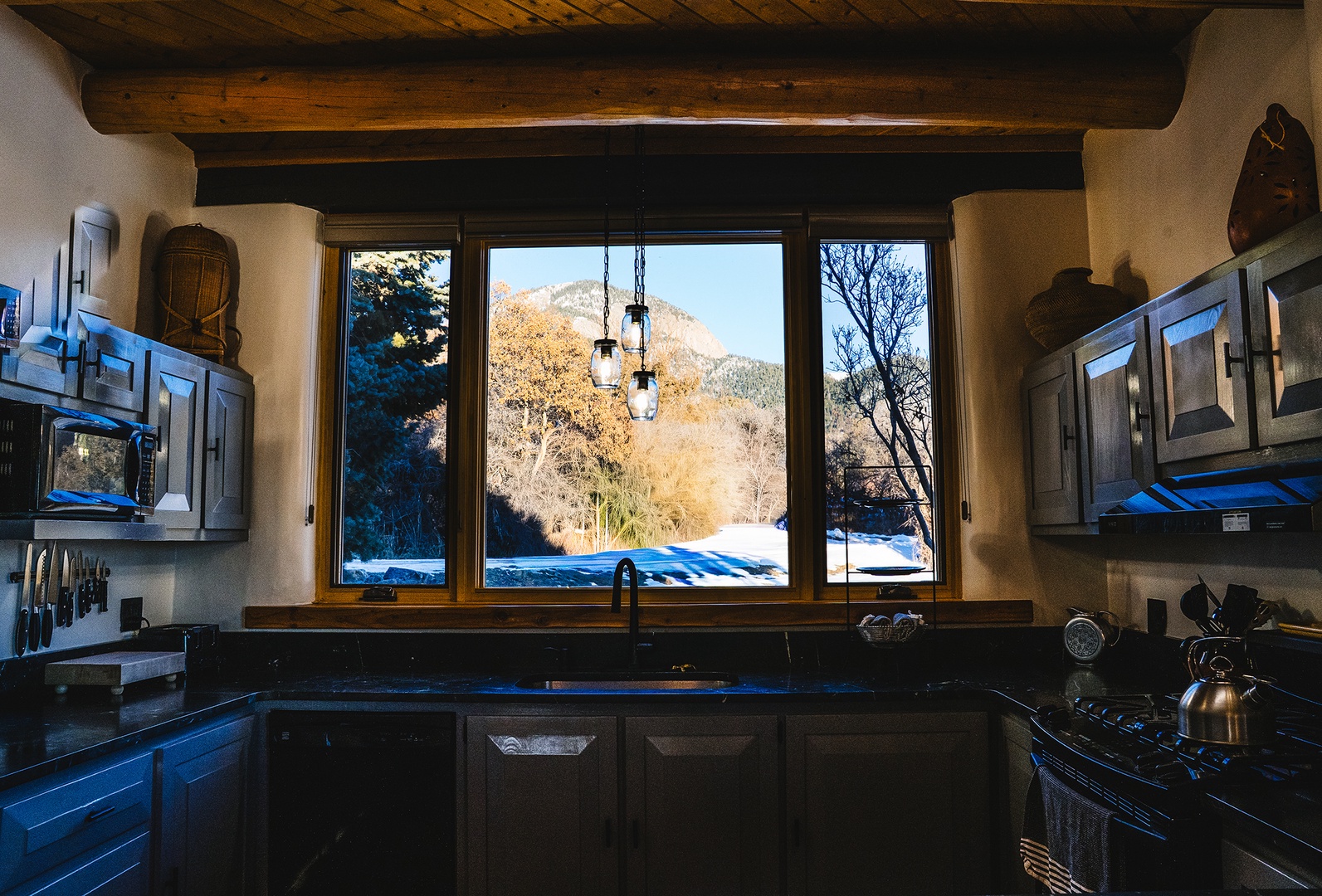Cook your meals while gazing at snow-capped mountains through this rustic kitchen's panoramic window, where exposed beams create authentic charm.