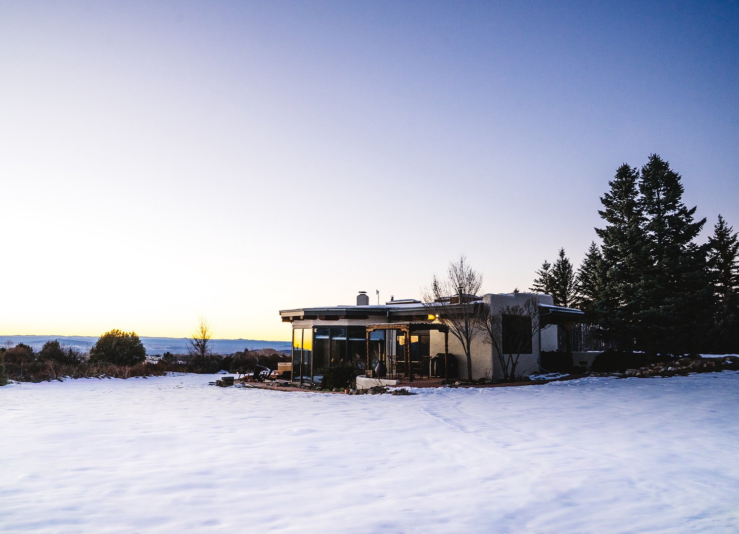 Modern property nestled in pristine winter landscape with mountain views and evergreen forest backdrop.