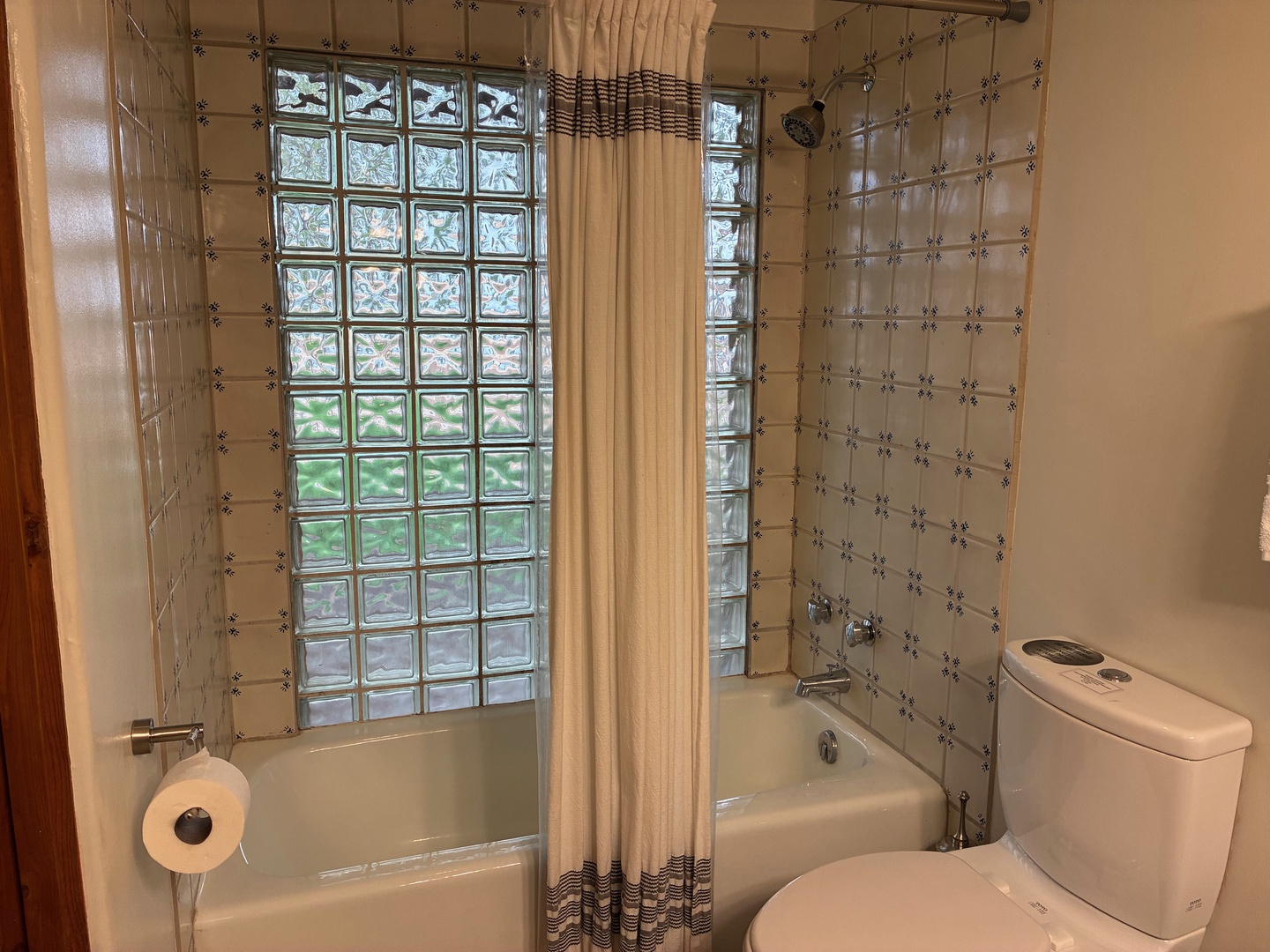 Your private bathroom features a tub-shower combo with crisp white tile, elegant glass block window letting in natural light, and fresh linens ready for your stay.