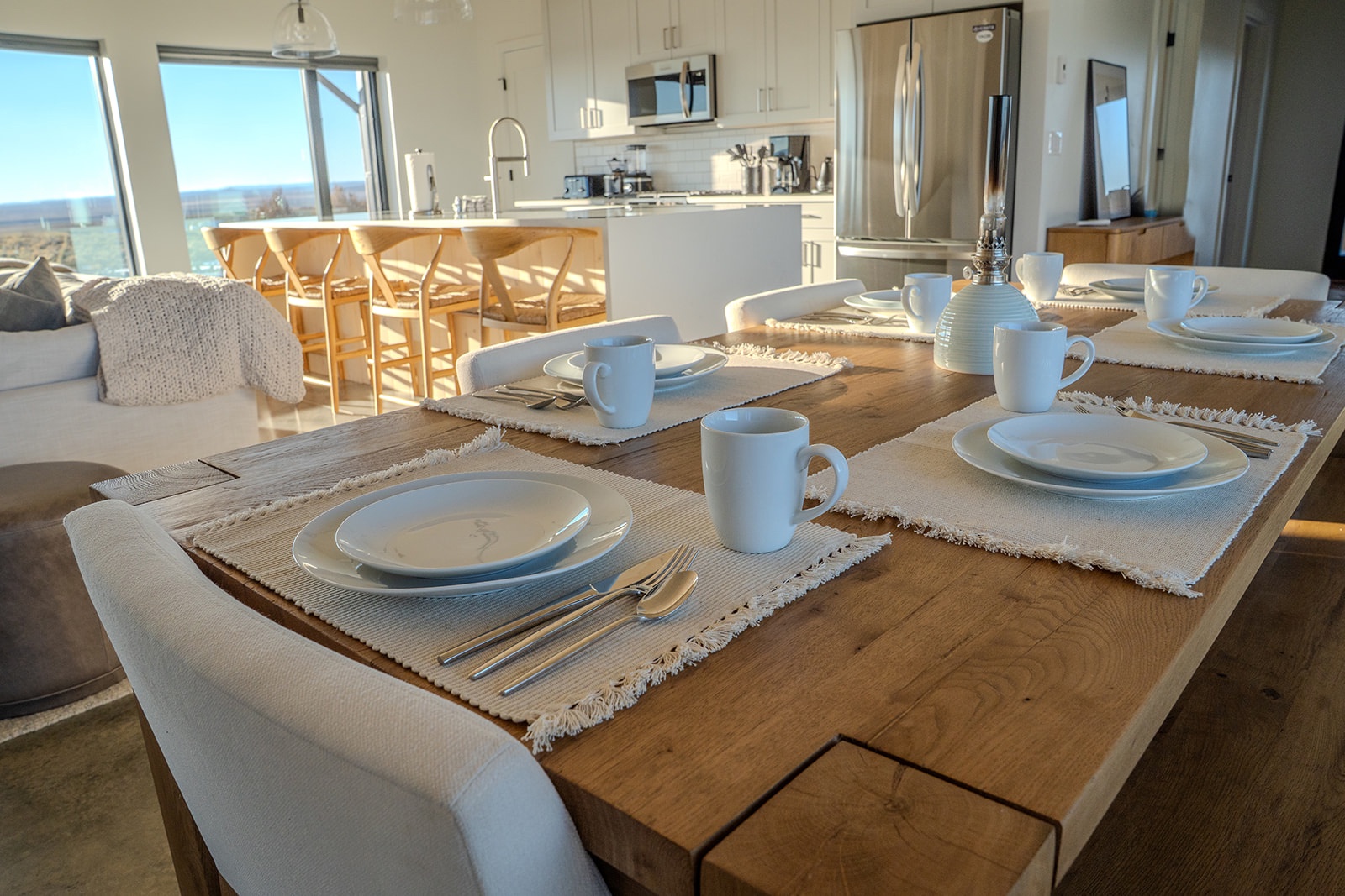 Your elegant dining table awaits with crisp white place settings, while the open kitchen invites culinary adventures in this sun-drenched modern space.