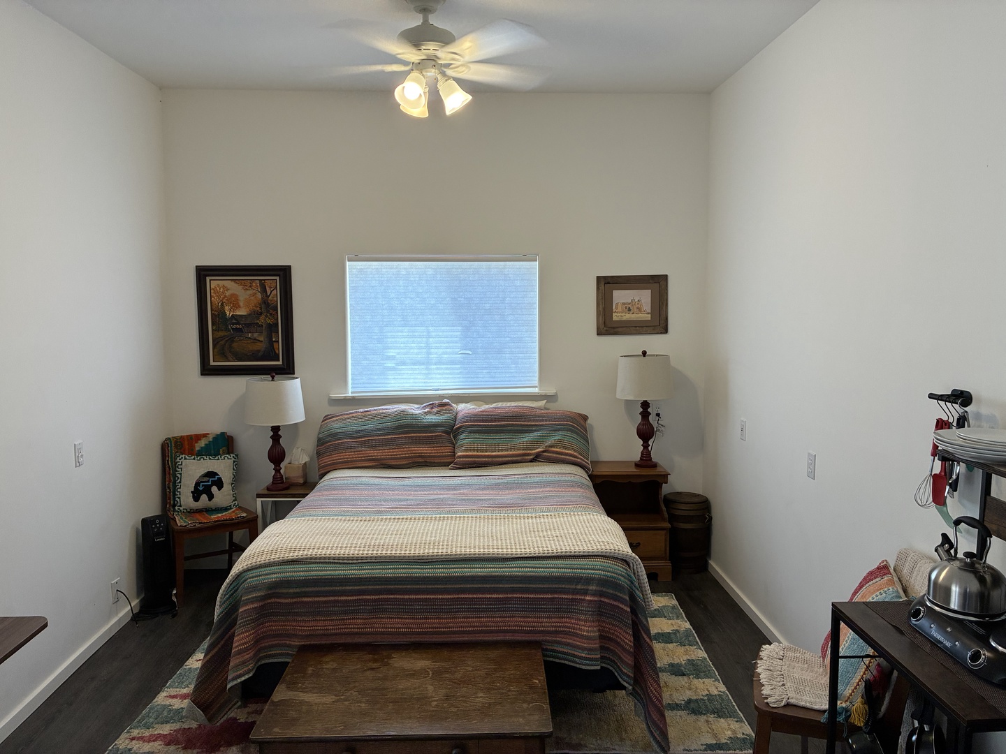 Your cozy bedroom retreat features a plush bed dressed in warm southwestern stripes, soft lighting from the ceiling fan above, and a peaceful window view to wake up to each morning.