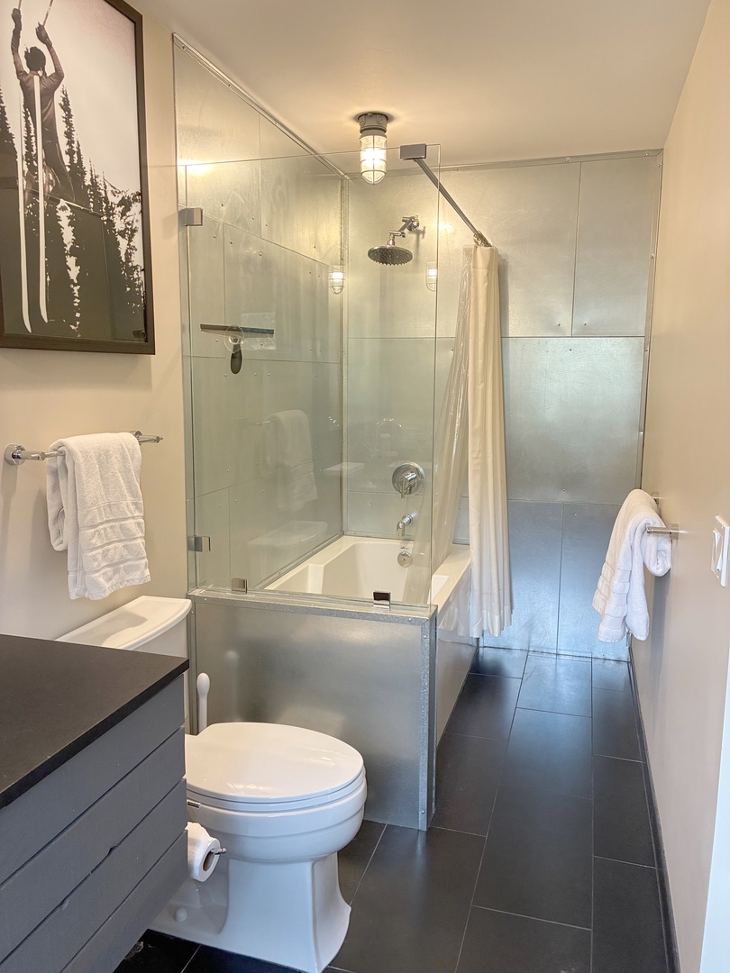 Unwind in your sleek modern bathroom with a spacious glass-enclosed tub and rainfall shower. Crisp white towels await, and the polished tile creates a spa-like escape.
