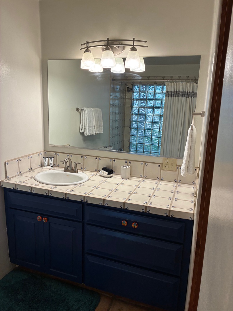 Bright and inviting bathroom with colorful tile countertops, plenty of storage in deep blue cabinets, and a glass-block shower to start your day feeling refreshed.