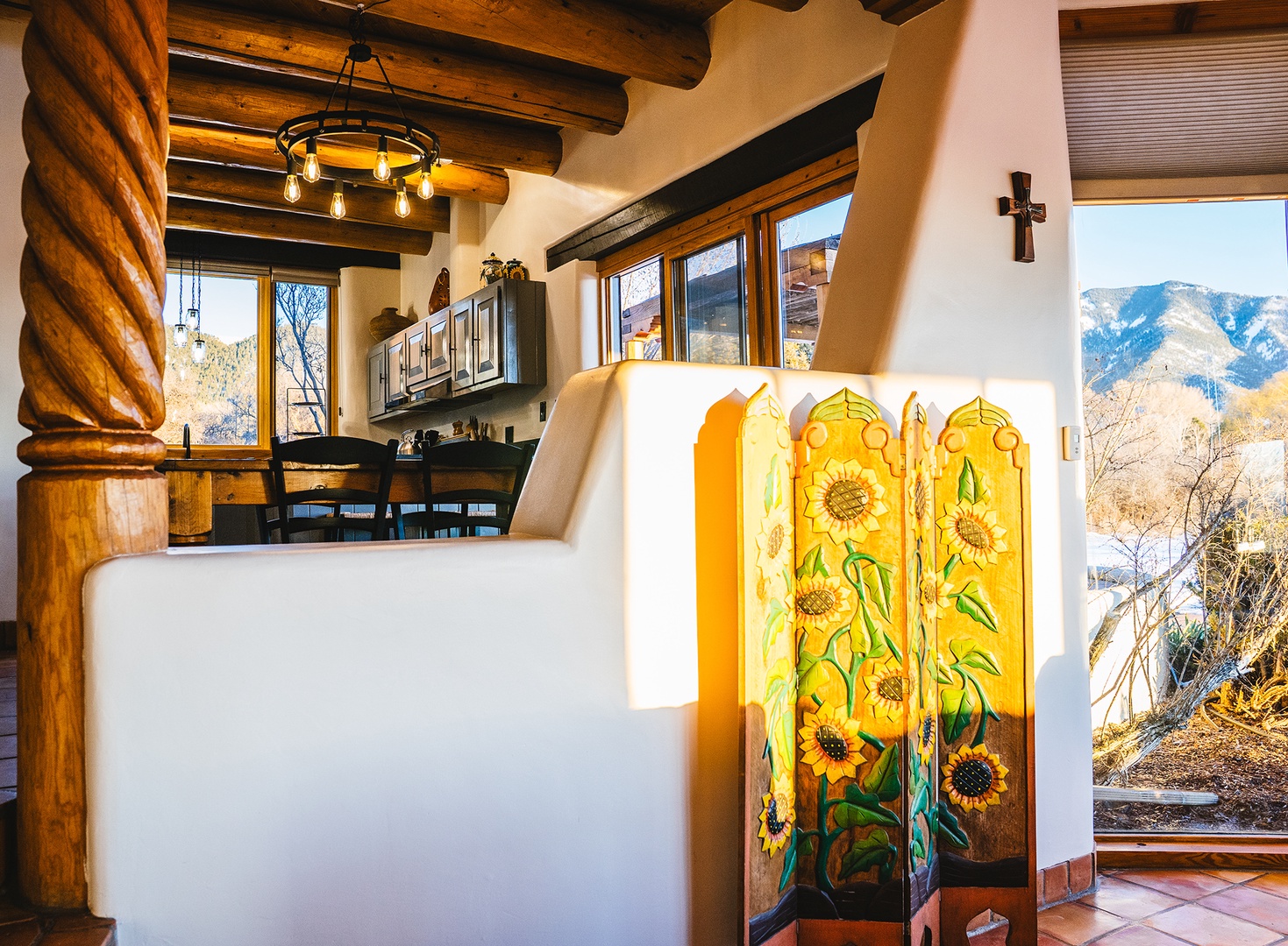 Relax in your rustic adobe retreat where handcrafted sunflower screens and exposed vigas frame stunning mountain vistas through expansive windows.