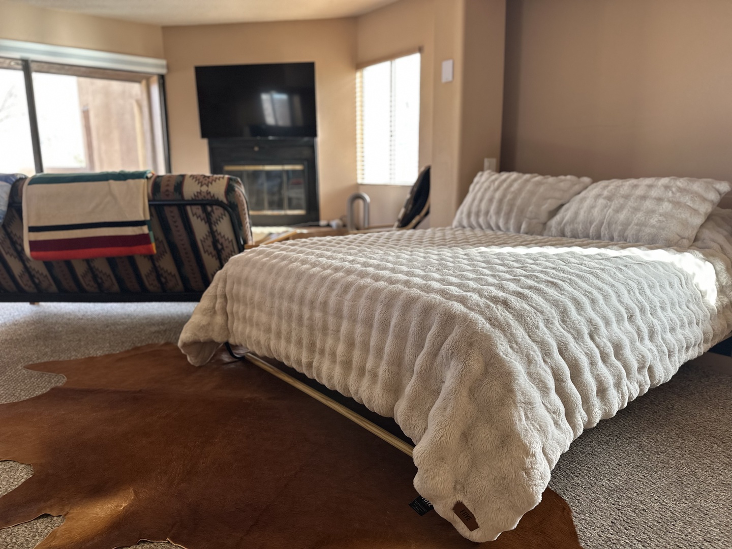 Sink into plush comfort with your oversized bed's luxurious textured bedding, while natural light streams through windows near the cozy fireplace.