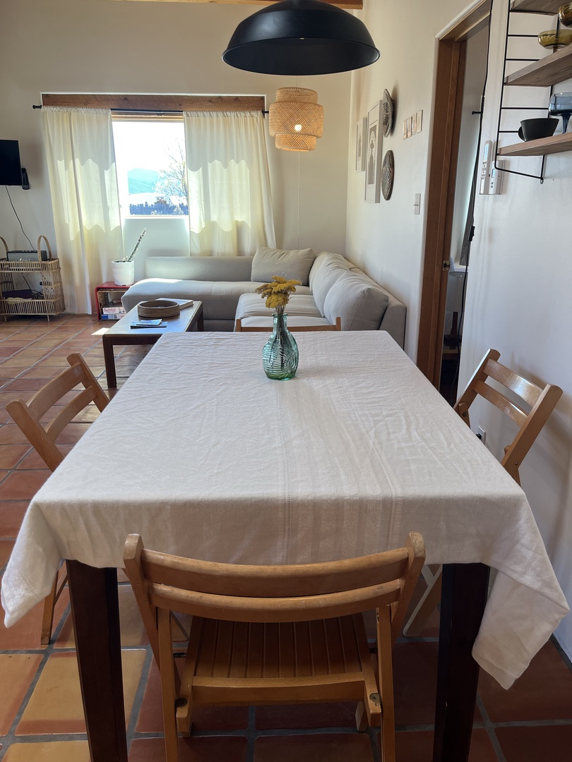 Gather around your bright dining table where warm sunlight streams through white curtains, creating the perfect space for meals and conversations.