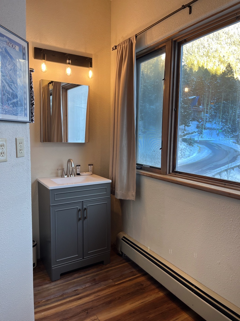 Refresh in your stylish bathroom featuring modern vanity, warm lighting, and stunning winter mountain views through large windows.