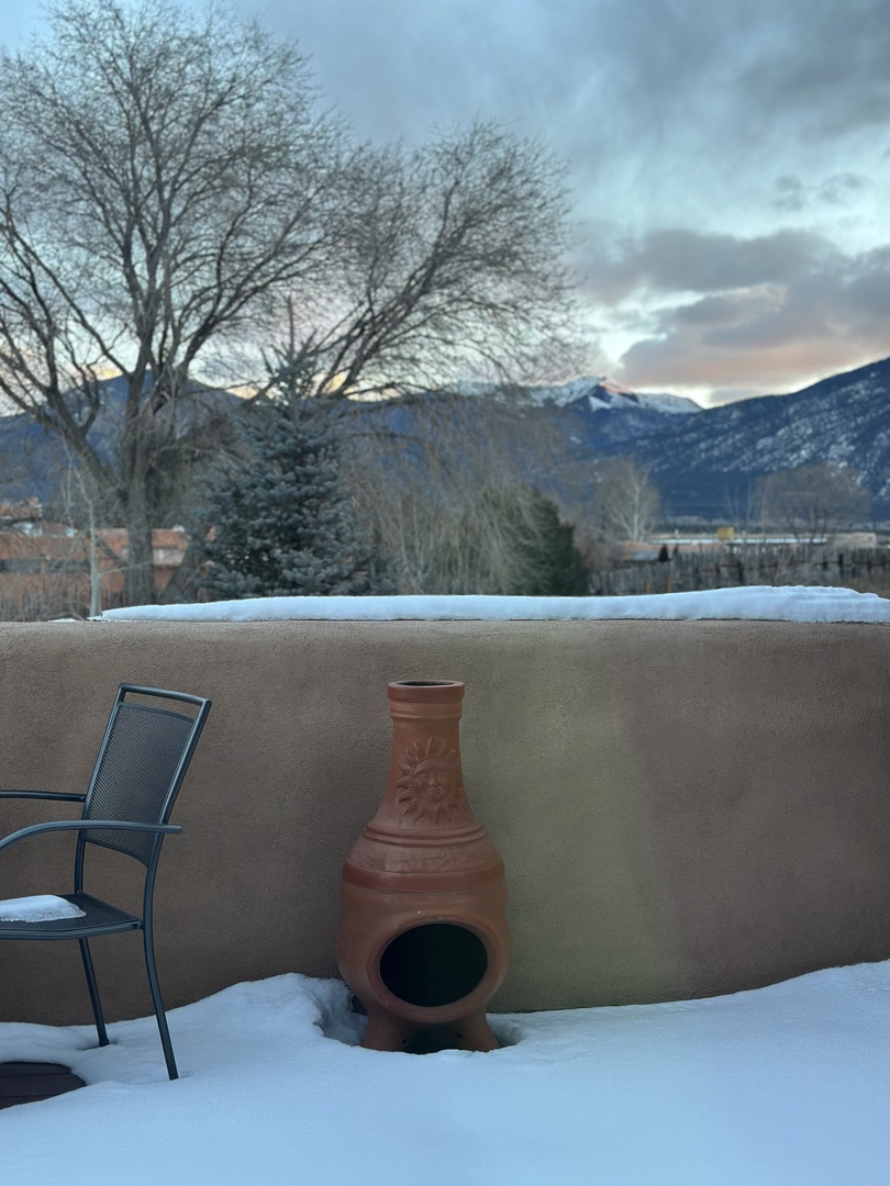 A snow-dusted patio with mountain backdrop offers a peaceful winter retreat. The outdoor chiminea and seating invite cozy evenings under open skies.