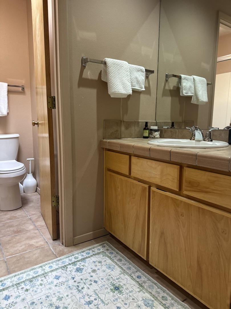 Step into your spacious bathroom with warm wood vanity, fresh towels, and thoughtful amenities waiting for your arrival.