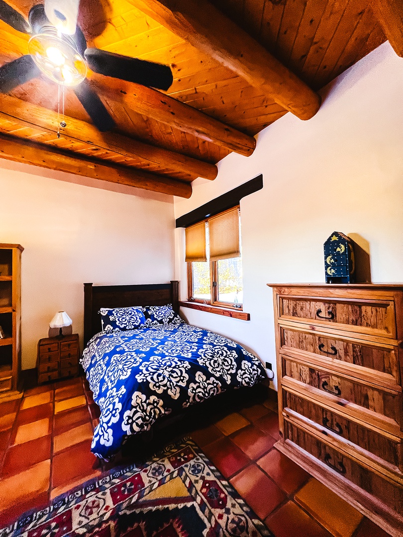 Rest under handcrafted wooden beams in your cozy bedroom, where rustic charm meets comfort with beautiful blue bedding and authentic tile floors.