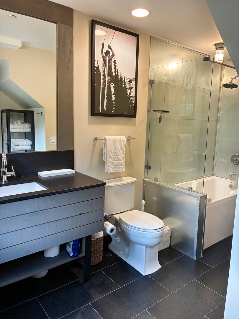Step into your sleek bathroom featuring a spacious glass-enclosed shower-tub combo, modern vanity, and mountain-inspired art that brings the alpine spirit right to your doorstep.