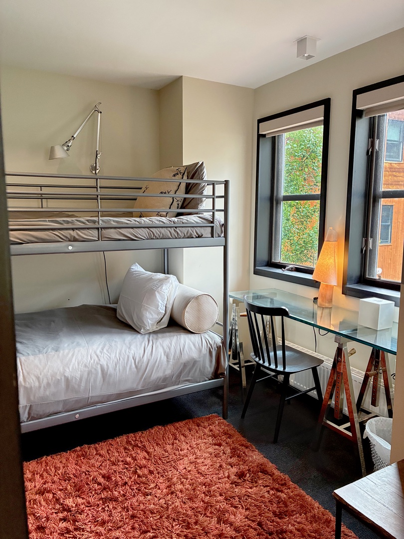Your cozy bunk bedroom awaits with soft linens and natural light streaming through large windows. A convenient desk and reading lamp create the perfect corner for planning your adventures.