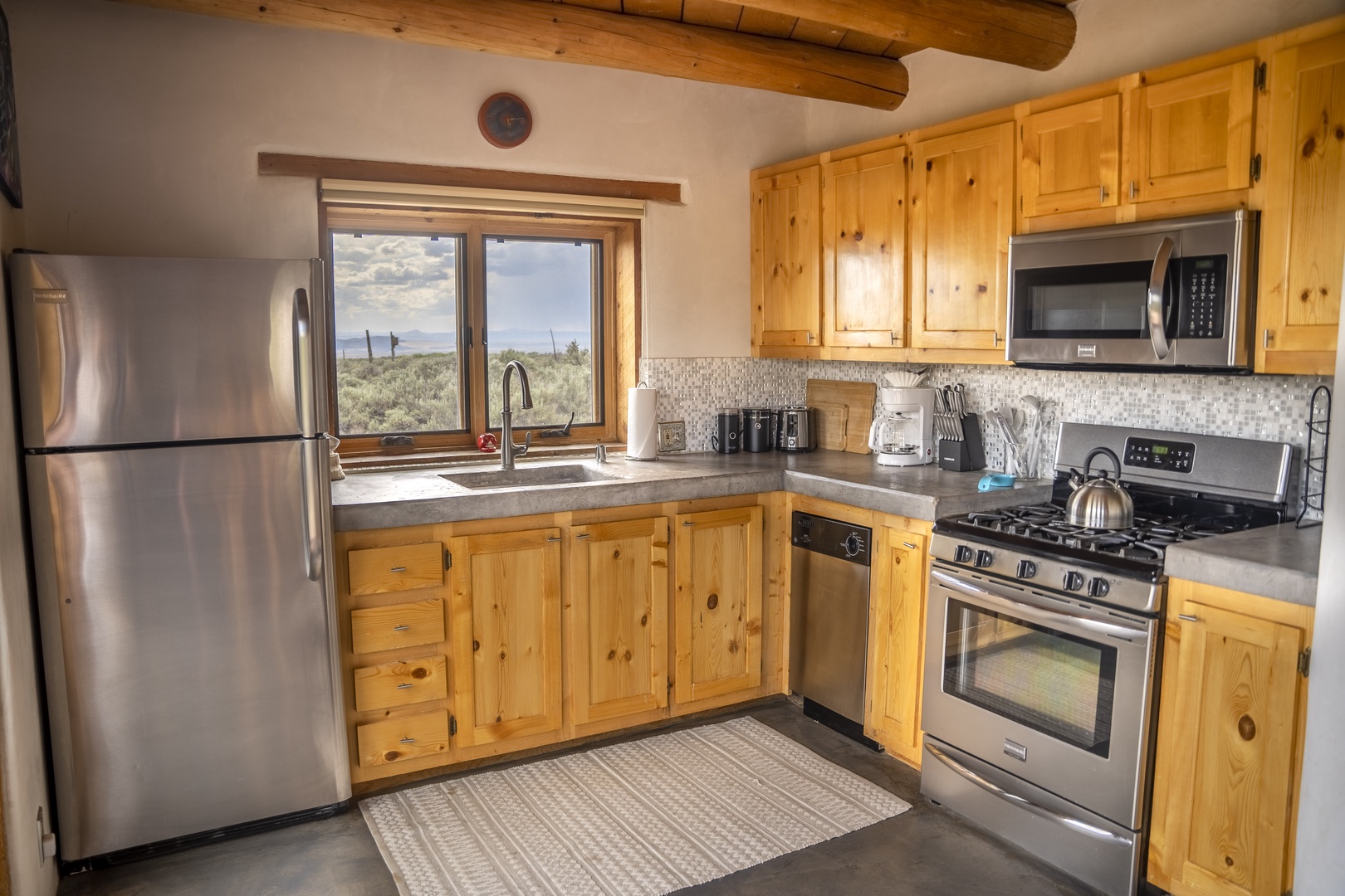 Your fully equipped kitchen features stainless appliances, warm knotty pine cabinetry, and a window framing peaceful desert views—perfect for preparing meals while soaking in the serene landscape.