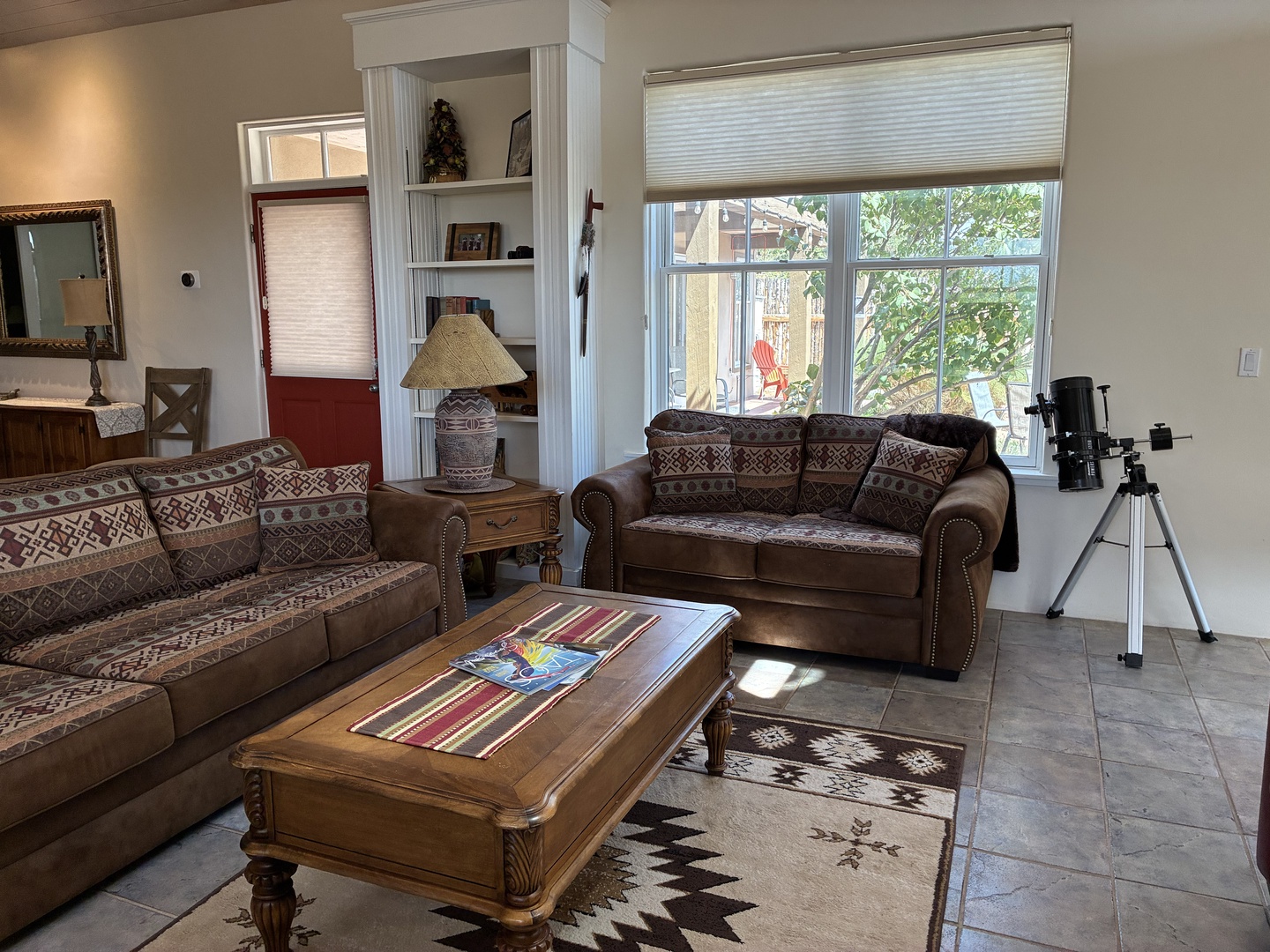 Relax in your spacious living area with comfortable seating, large windows bringing in natural light, and a charming glimpse of the peaceful backyard garden through the window.