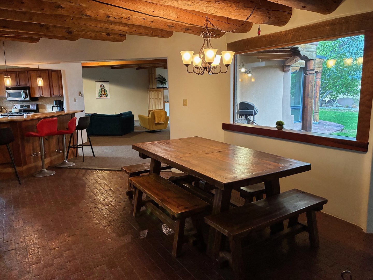 Gather around the handcrafted wood dining table under warm rustic beams, where meals become memories. The open layout connects you to the full kitchen and cozy seating, while large windows frame views of your private garden and BBQ patio.
