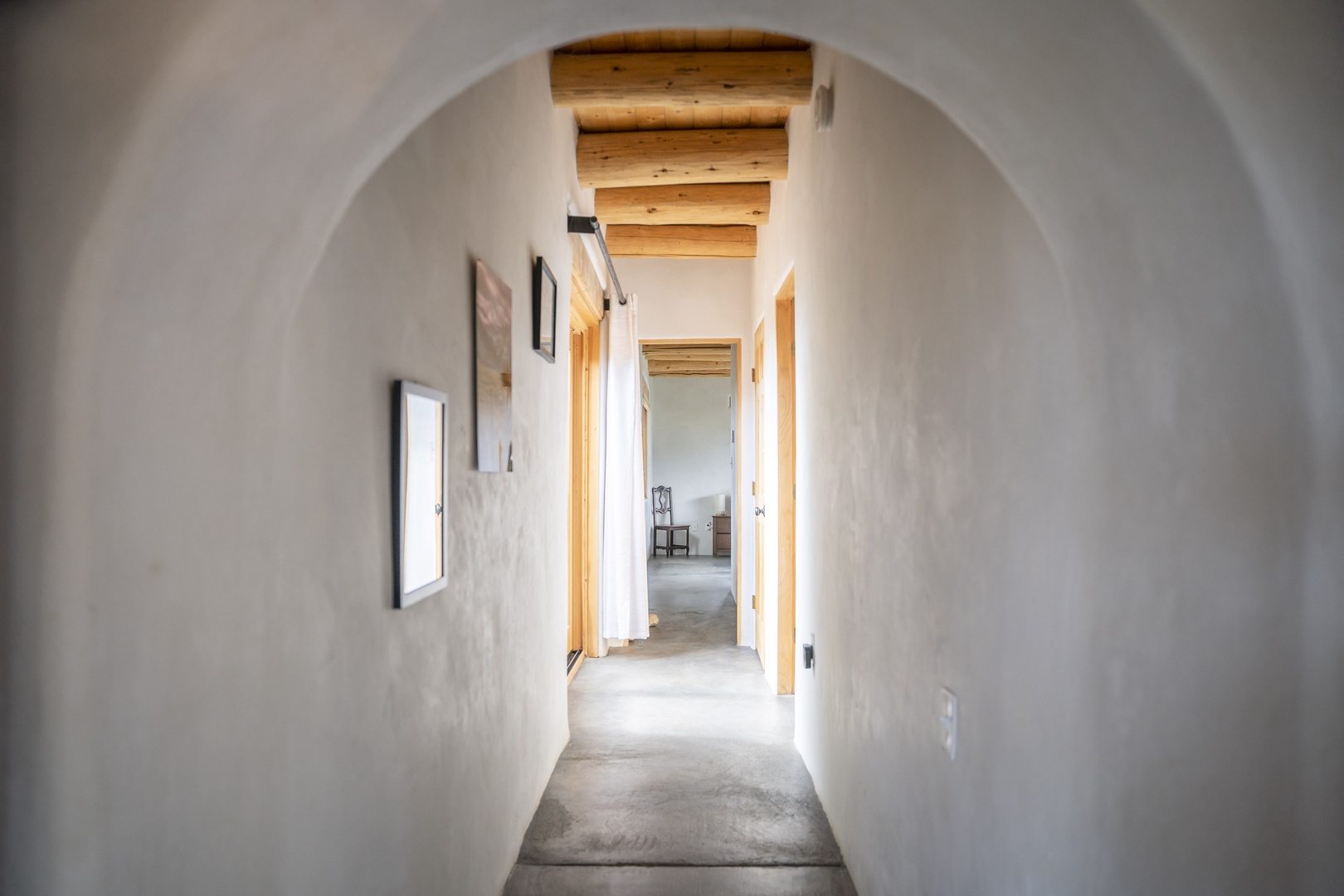 Elegant archway frames your private hallway, where rustic wood beams meet minimalist design and soft natural light guides you through this sweet retreat.