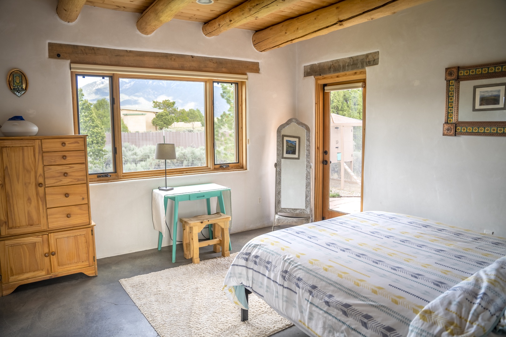 Drift off in your bright bedroom with authentic viga ceilings and a private door to your outdoor space. Natural light floods in through large windows framing garden views, while handcrafted wood furnishings add Southwest charm.