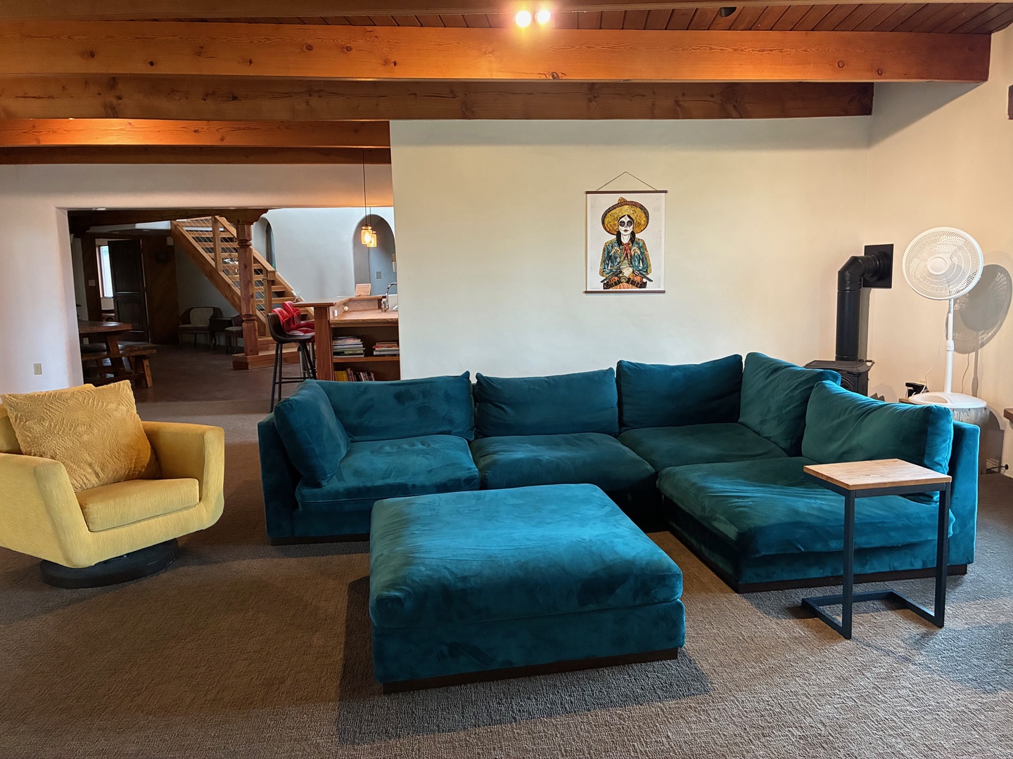 Settle into the plush teal sectional and feel instantly at home beneath warm wooden beams. The open layout invites you to unwind, with a cozy yellow chair and plenty of space to gather with loved ones.