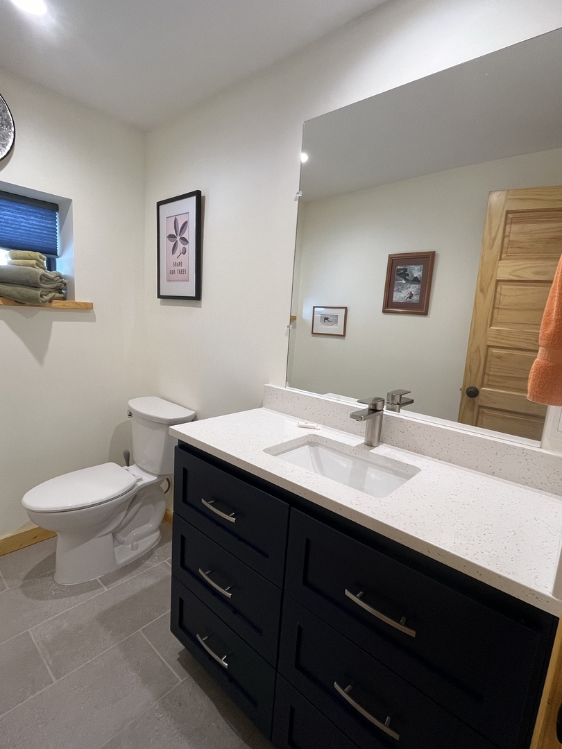 A crisp, modern bathroom awaits you with sleek navy cabinetry, gleaming white countertops, and thoughtful touches like fresh towels ready for your stay.