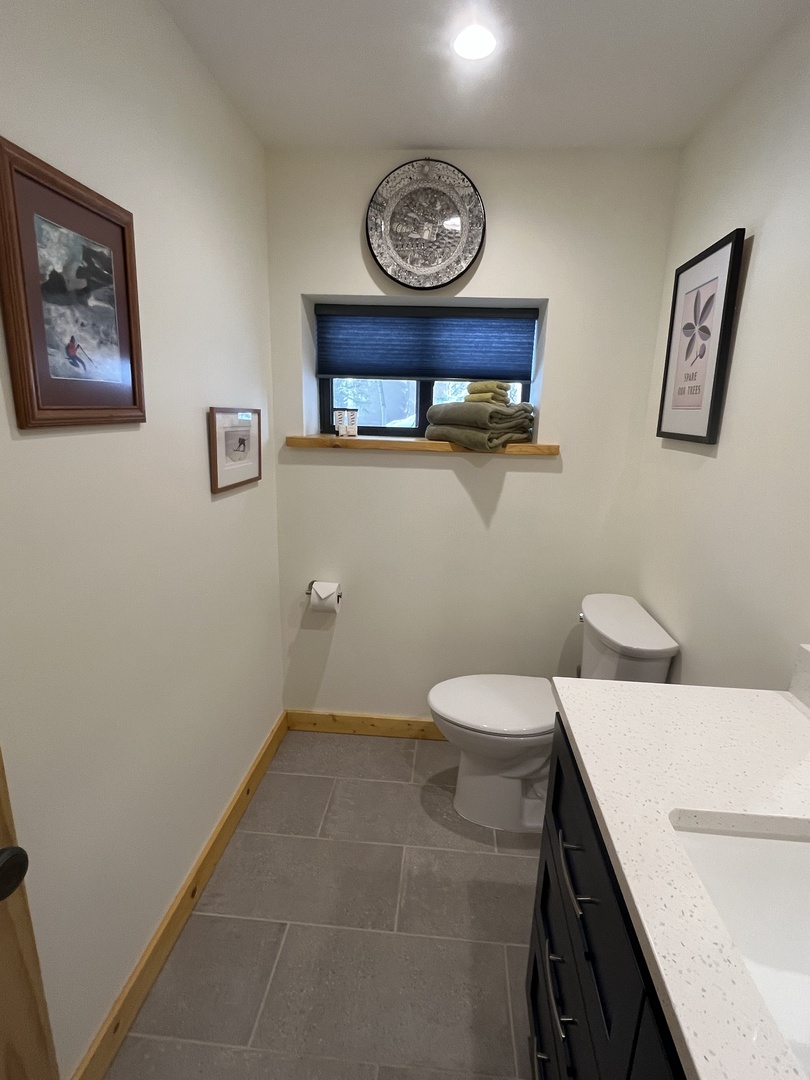 A clean, modern bathroom with ski-themed artwork and fresh towels awaits. The window ledge provides natural light and a glimpse of the outdoors beyond.
