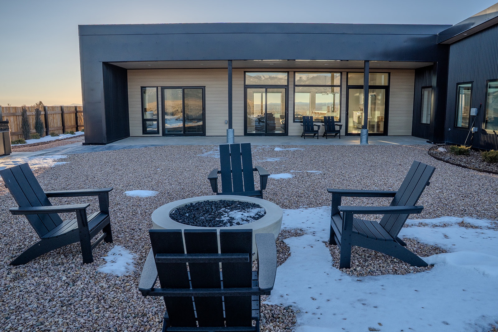 Modern property exterior featuring expansive glass windows and outdoor seating area with fire pit surrounded by winter landscape.