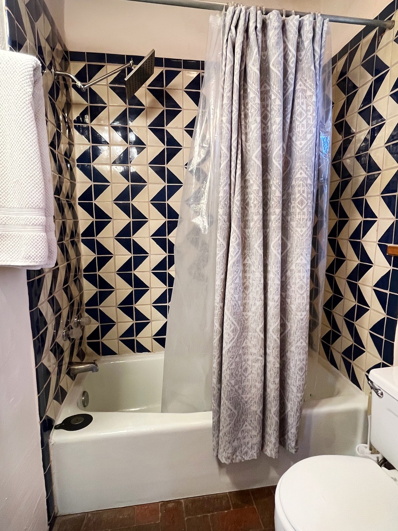 Step into your private bathroom featuring a striking geometric tile pattern and a refreshing tub-shower combo, complete with plush towels waiting for you.