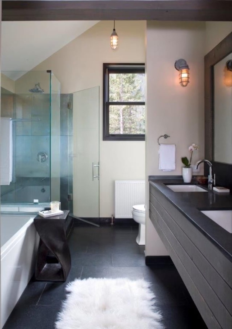 Your spa-like bathroom features a sleek dual-sink vanity, glass-enclosed shower, soaking tub, and natural light streaming through the window—perfectly designed for unwinding after a day of adventure.