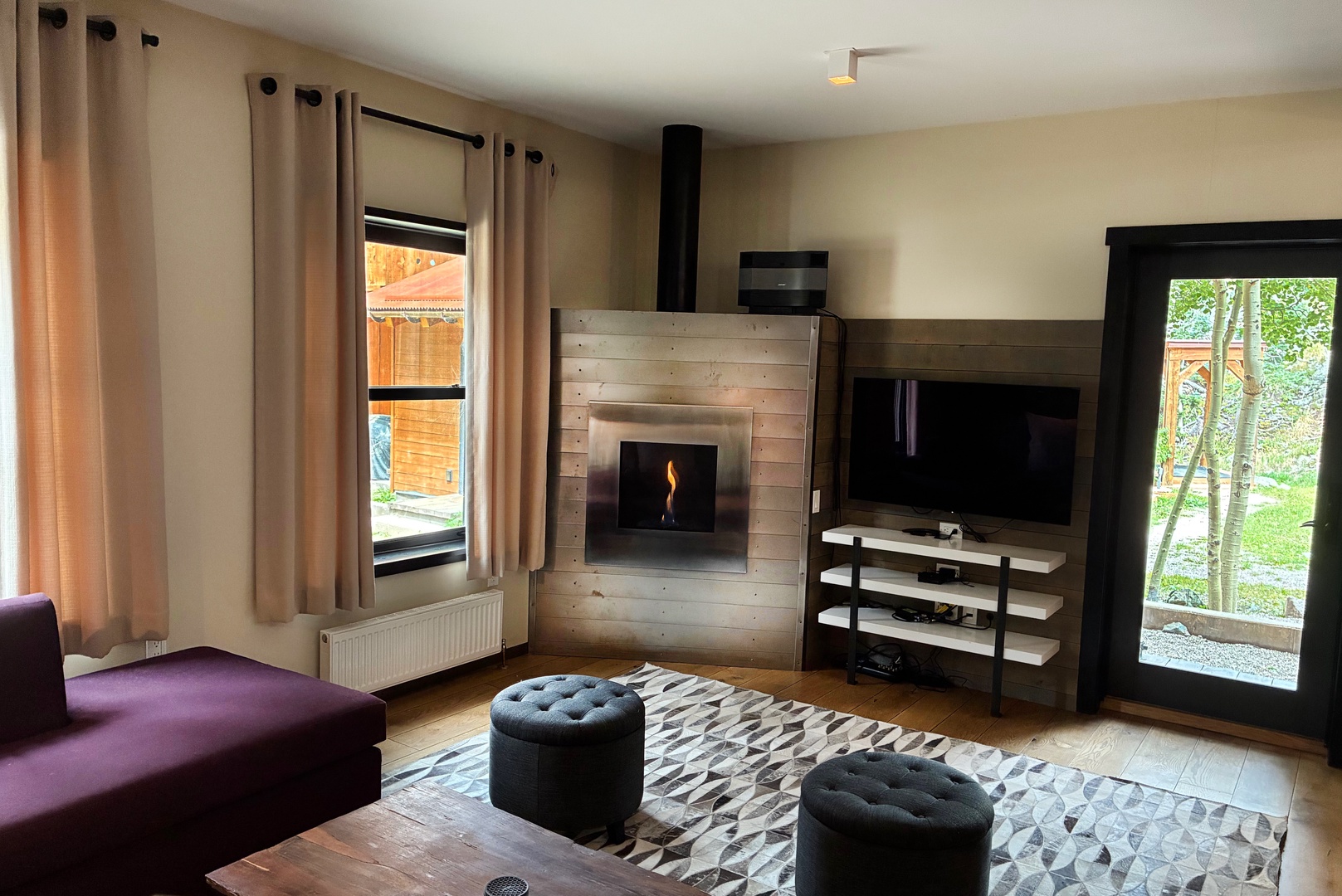 Cozy up in your stylish living room with a warm fireplace, flat-screen TV, and natural light streaming through large windows overlooking the garden. Perfect for relaxing after a day of adventure.