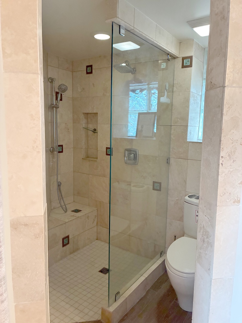 Your private bathroom features a spacious walk-in shower with elegant tile work, a built-in bench, and plenty of natural light streaming through the skylight above.