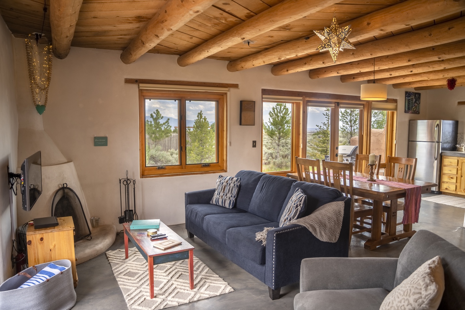 Sink into comfortable seating beneath exposed wooden beams as natural light pours through expansive windows framing beautiful desert scenery. Your cozy gathering space flows into a welcoming dining area and well-equipped kitchen.