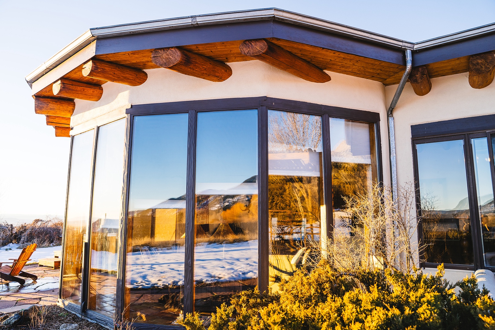 Modern property featuring distinctive architectural design with exposed wooden beams and expansive floor-to-ceiling windows overlooking snowy mountain landscape.