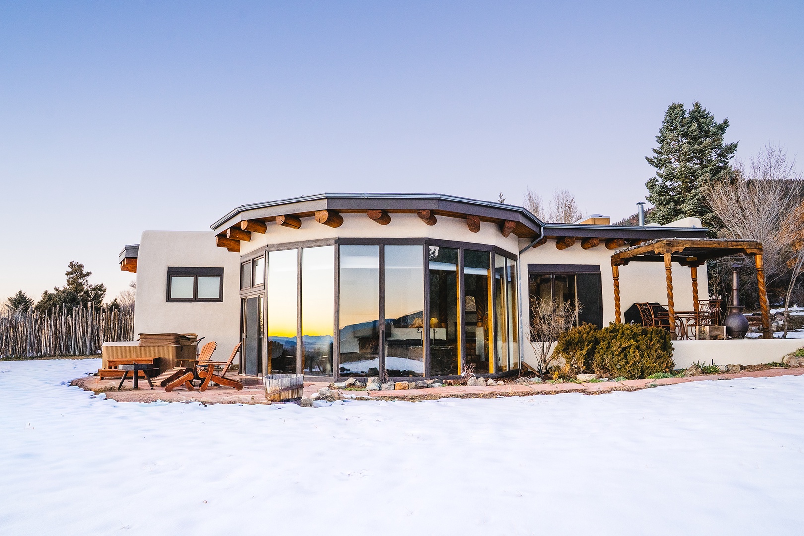 Modern retreat with curved glass design surrounded by snow-covered landscape and mountain views.