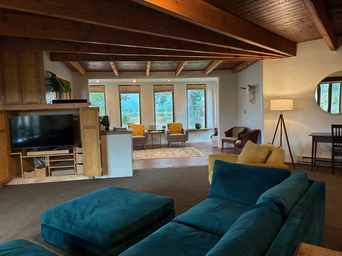 Step into your spacious retreat where soaring wood-beam ceilings frame a light-filled living space. Sink into the plush teal sofa and let your eyes wander through sunlit windows to the serene water views beyond.