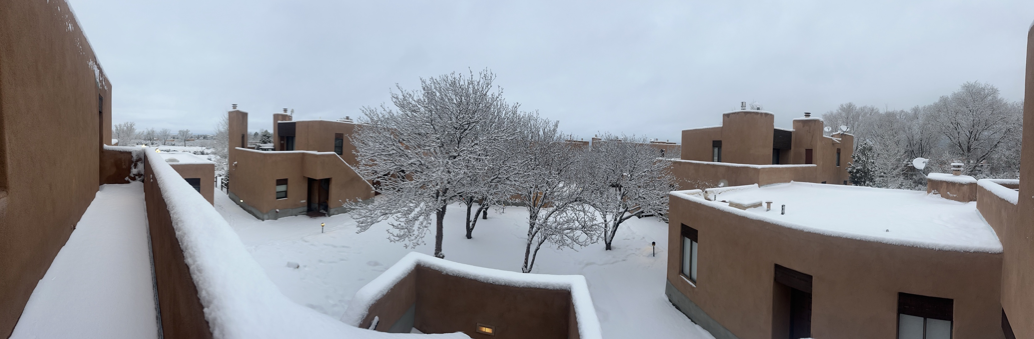 Snowy day view of adobe-style buildings and bare winter trees from the deck.
