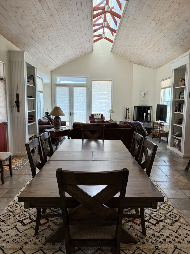 Gather around the dining table or relax in the living room beneath soaring wood-planked ceilings and a stunning skylight. Natural light fills the space, inviting you to unwind and feel right at home.