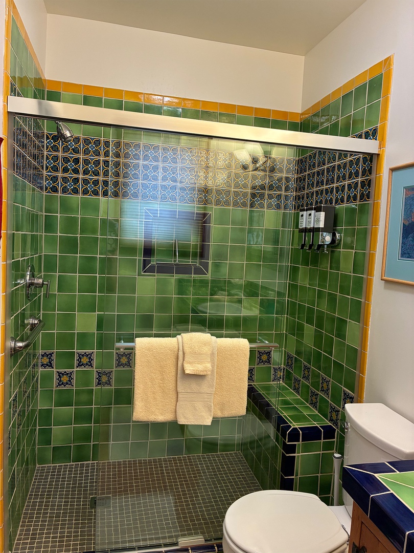 Step into your private bathroom featuring vibrant hand-painted tiles in emerald green and gold, complemented by intricate decorative accents and plush towels waiting for you.