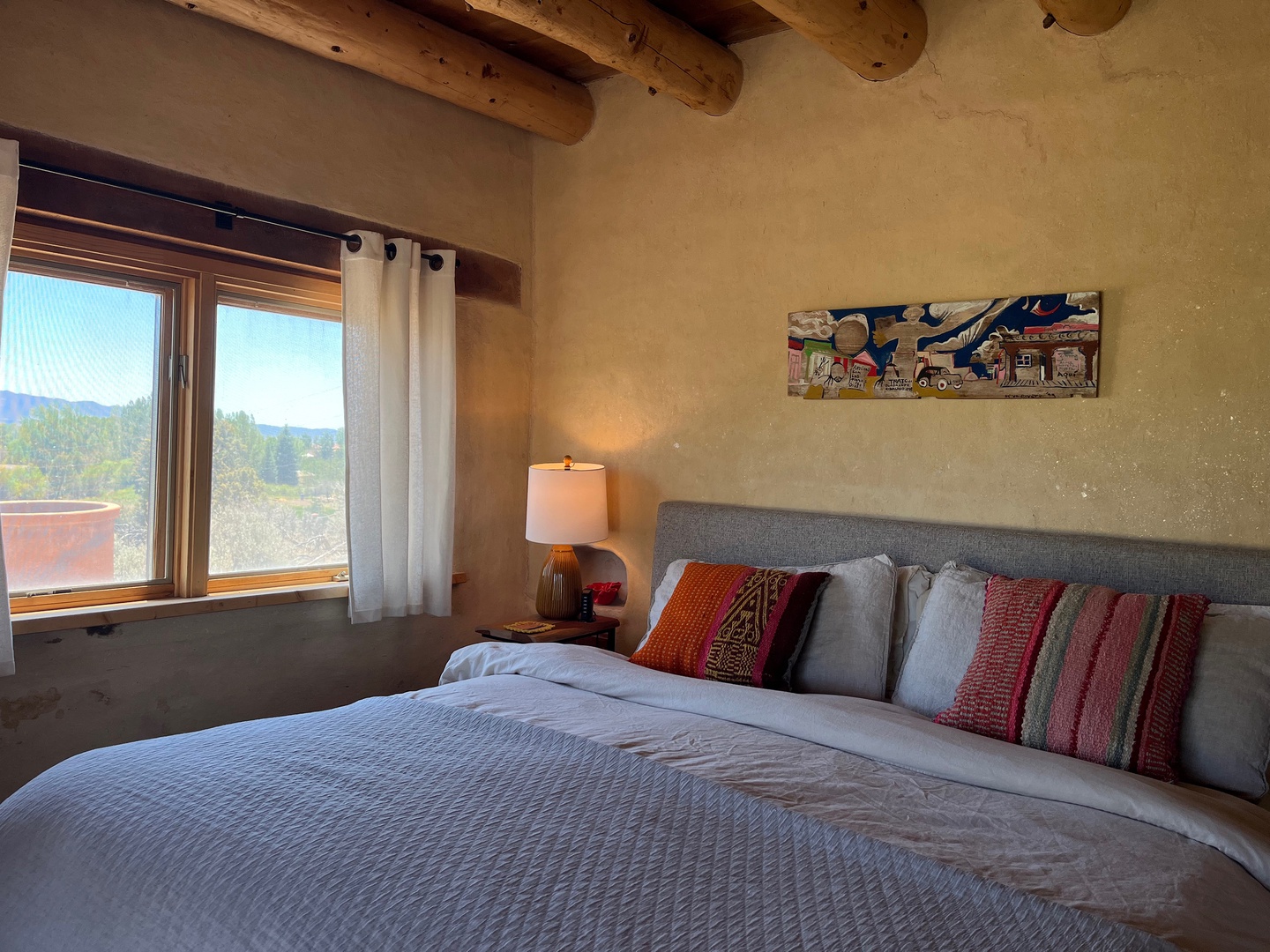 Wake to sweeping mountain views from your bed. This cozy bedroom features rustic exposed beams, soft bedding, and warm desert tones.