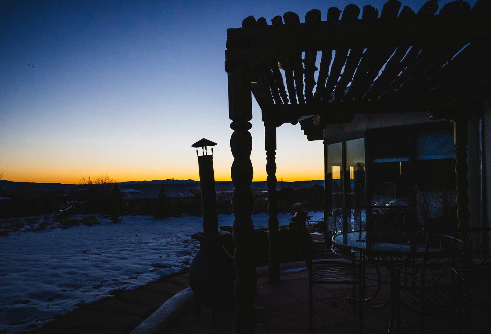 Property's covered patio overlooks snow-covered landscape at sunset, offering peaceful mountain views and outdoor seating area.