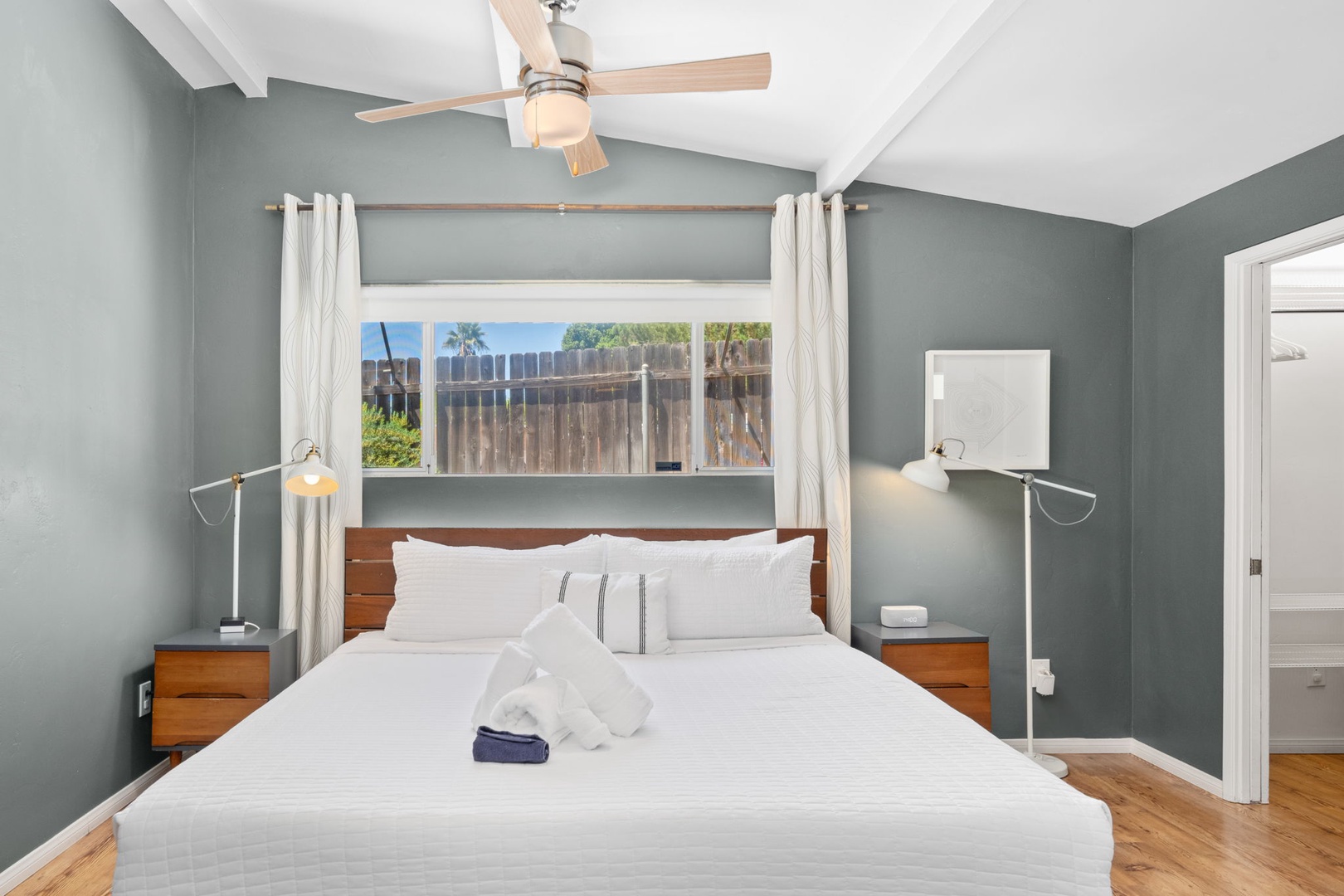 Sink into crisp white linens and wake to soft natural light in this serene primary bedroom. Mid-century wood furnishings and curated art warm calming sage walls, creating your peaceful retreat. Private ensuite bathroom and walk in closet.