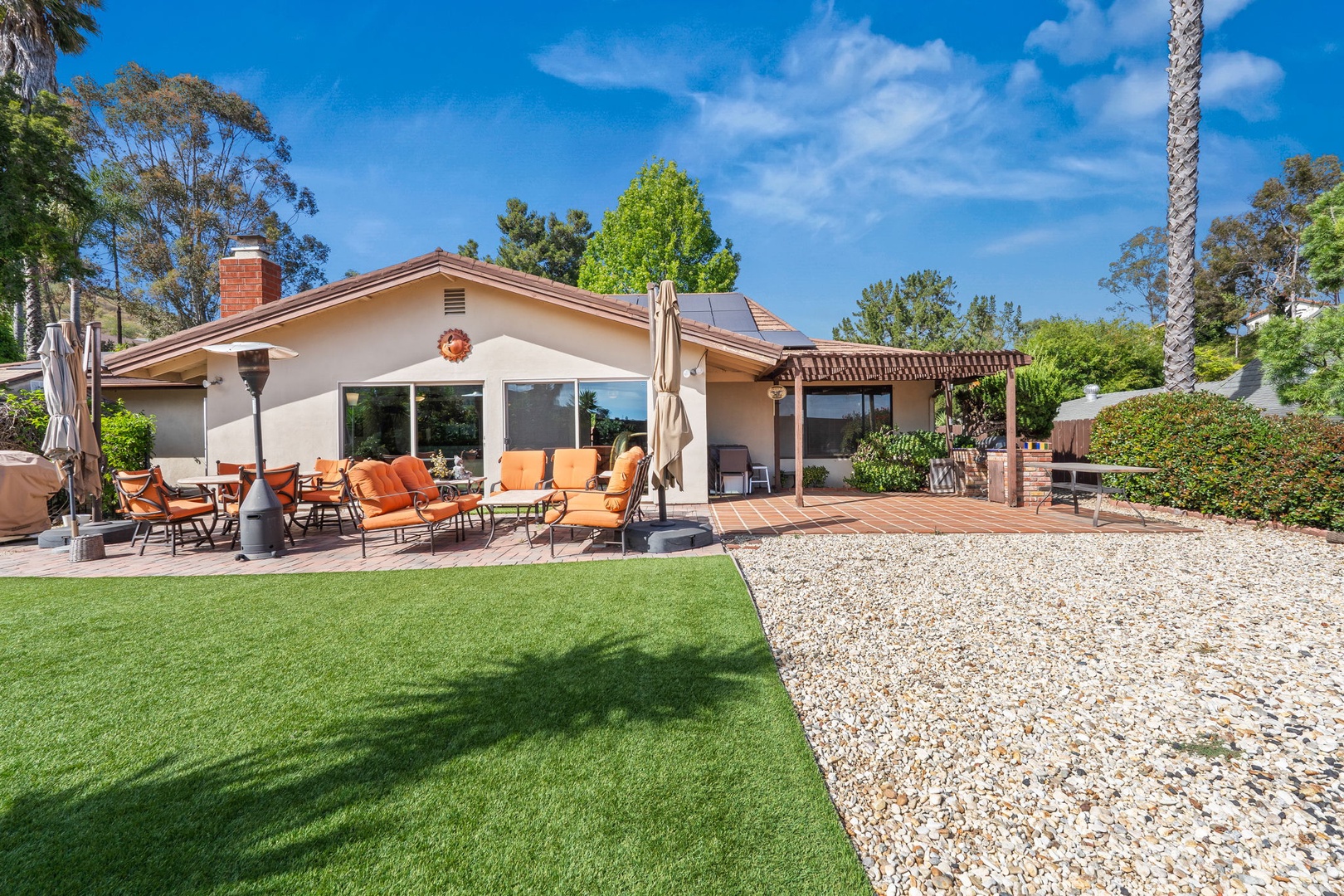 Modern single-story vacation home featuring spacious outdoor entertaining areas with patio furniture, barbecue facilities, and manicured landscaping in a peaceful residential setting.