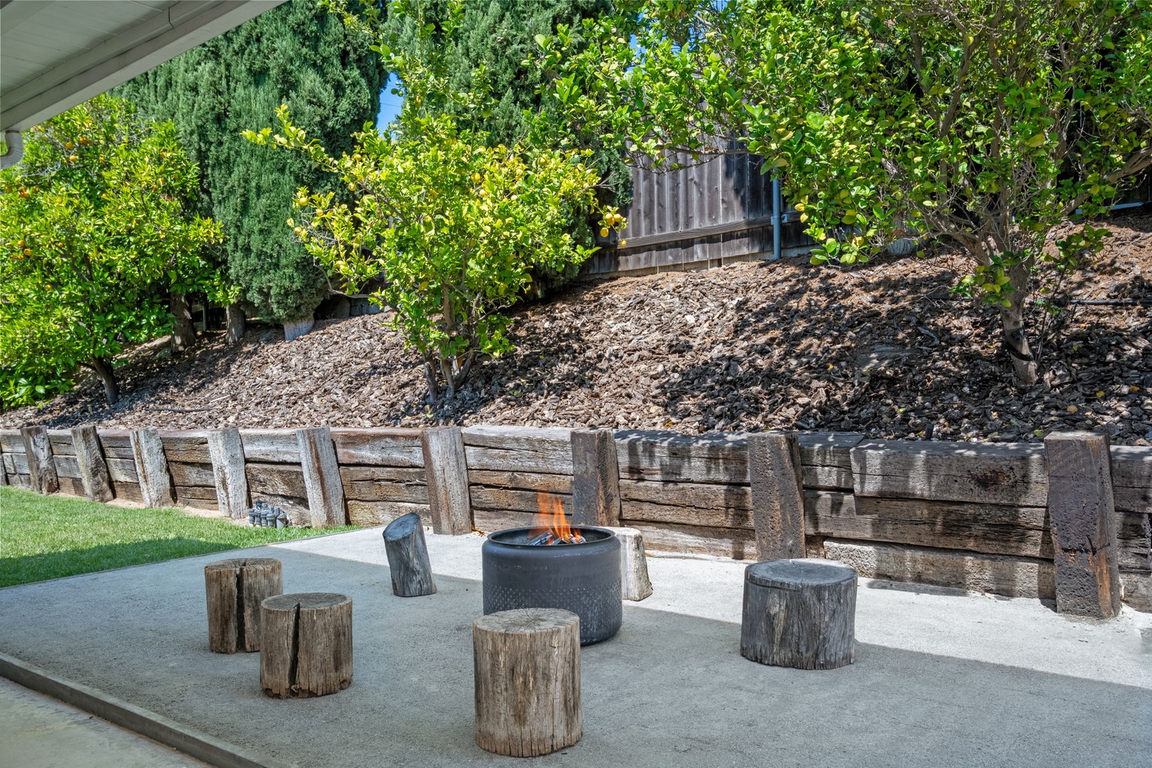 Gather around the modern fire pit on this serene patio, surrounded by rustic log seating and terraced gardens. A perfect spot to relax under the trees and enjoy warm evenings outdoors.