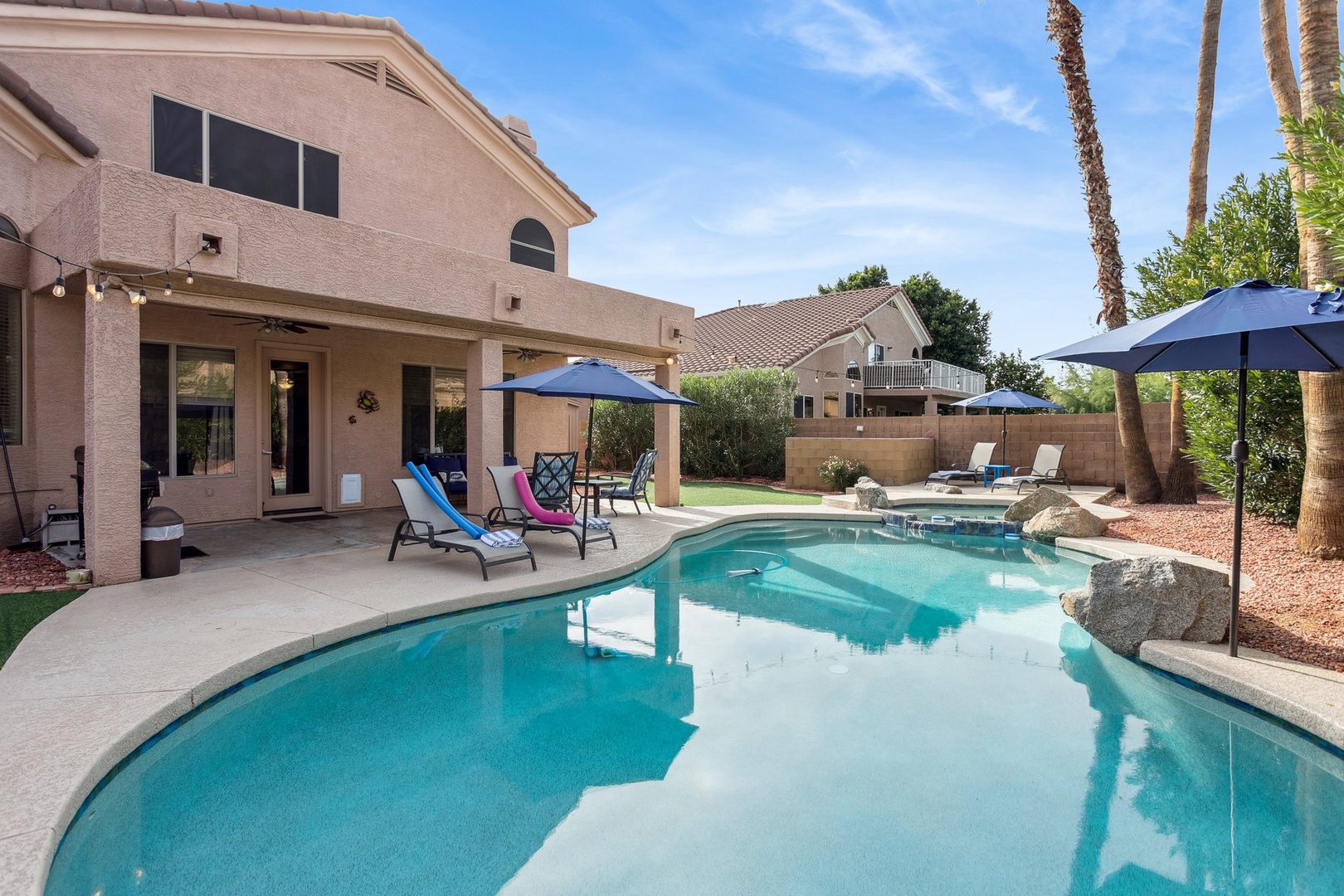 Modern home features sparkling pool with sunny patio, lounge chairs, and tropical landscaping in a peaceful residential setting.