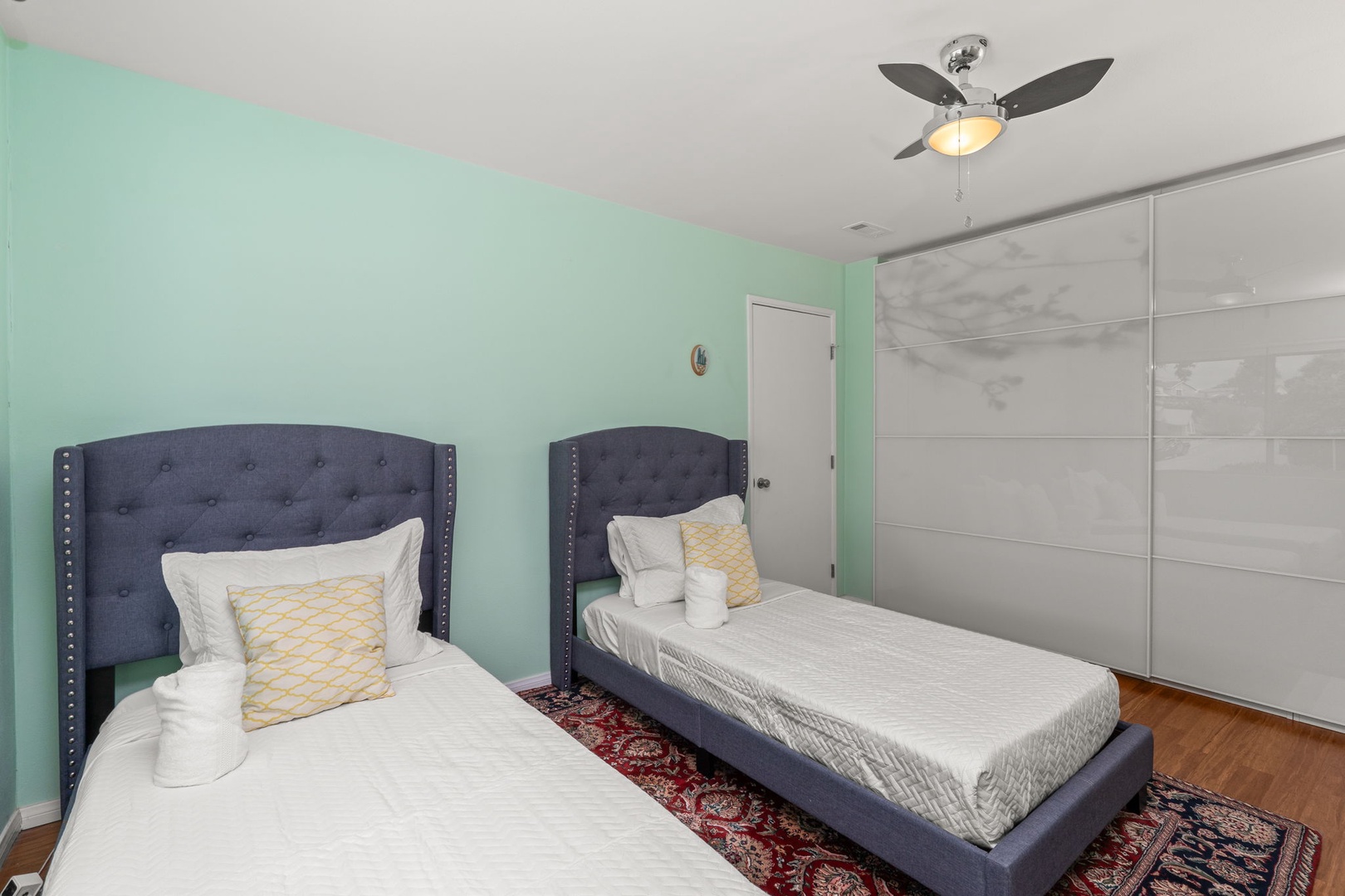 Relax in your serene twin bedroom with plush upholstered headboards, fresh mint walls, and elegant mirrored wardrobes for ample storage.