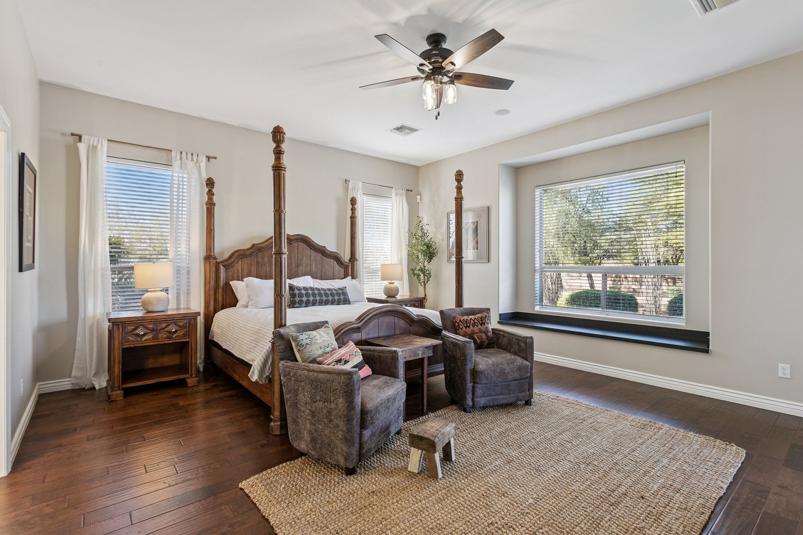 Unwind in your elegant primary suite with four-poster bed, cozy seating area, and peaceful views through multiple windows.