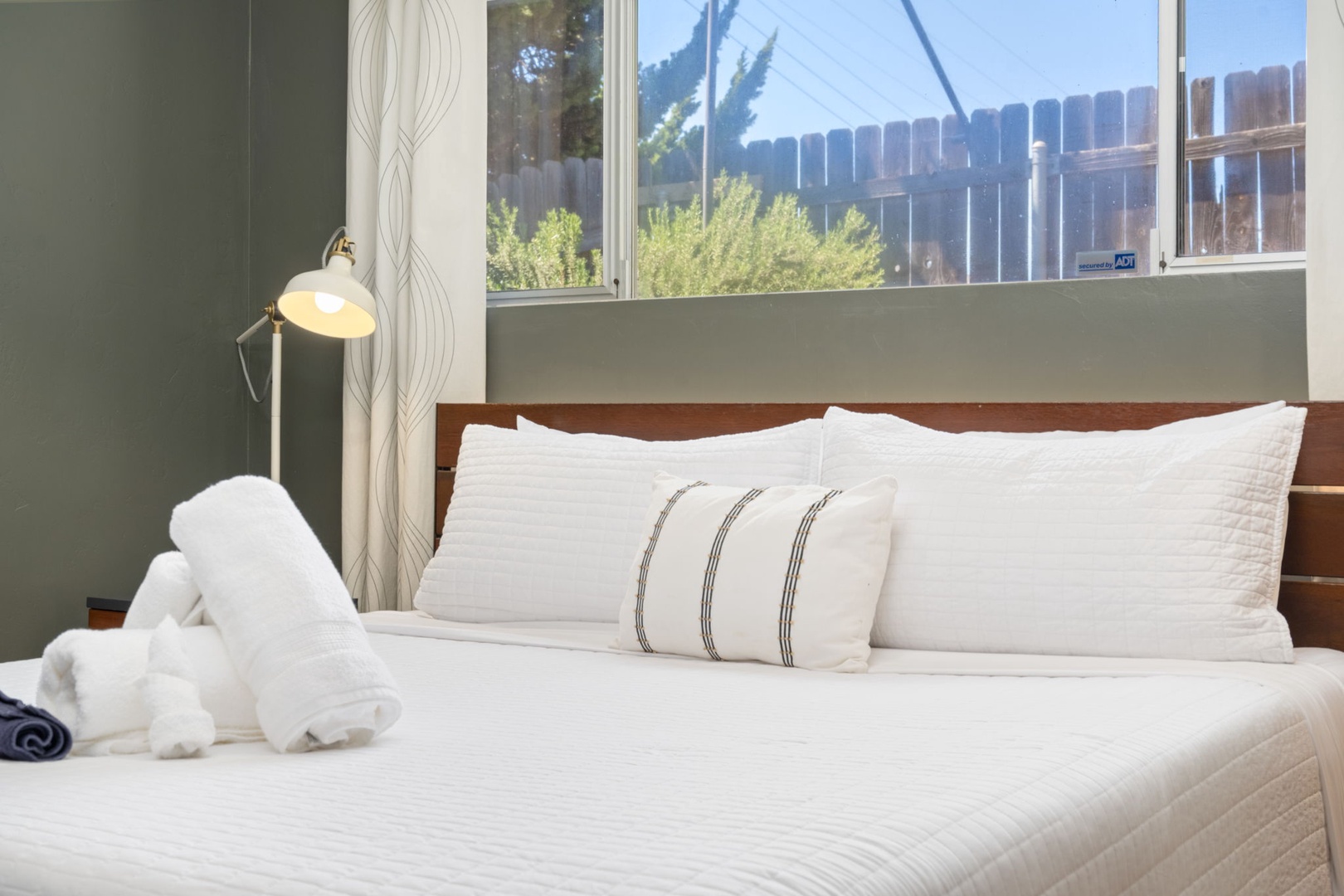 Sink into crisp white linens and wake to soft natural light in this serene primary bedroom. Mid-century wood furnishings and curated art warm calming sage walls, creating your peaceful retreat. Private ensuite bathroom and walk in closet.